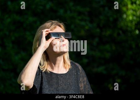 A woman is wearing black protective glasses to observe the upcoming solar eclipse Stock Photo