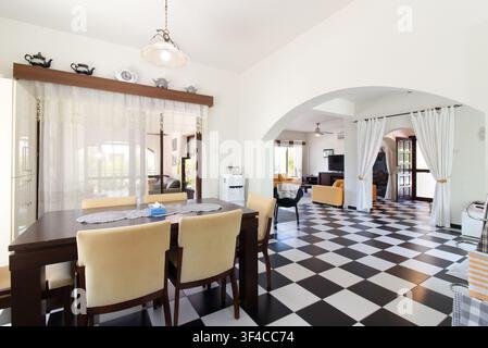 Spacious open-plan home interior featuring a dining area with a dark wood table and cream chairs, stylized black-and-white checkered tiled flooring Stock Photo