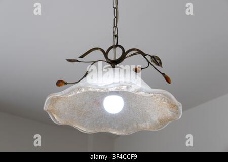 An elegant vintage-style hanging ceiling light fixture featuring a textured frosted glass shade with scalloped edges, decorative metal leaf accents Stock Photo