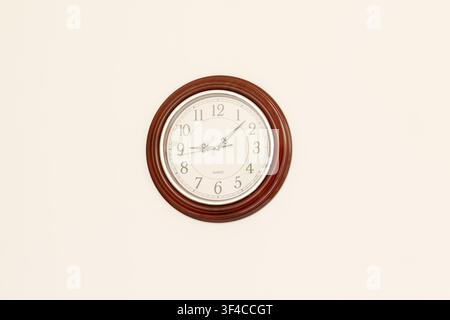 Classic round wooden wall clock with a white dial and black Arabic numerals mounted on a plain wall Stock Photo