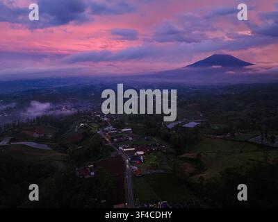 Aerial view of Darajat Pass at dusk with a dramatic purple and pink sunset sky over the mountain landscape, lush green hills, and the small town of Ke Stock Photo