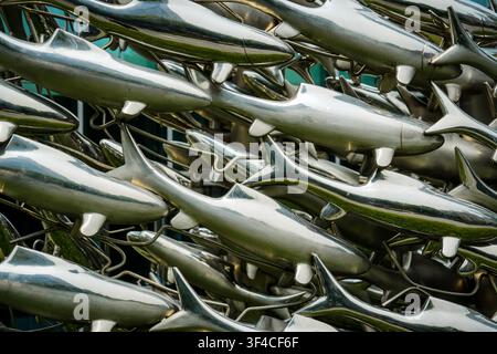 A dense arrangement of polished silver-colored stainless steel fish figures fills the frame, each approximately 30-40 cm long with smooth, rounded bod Stock Photo