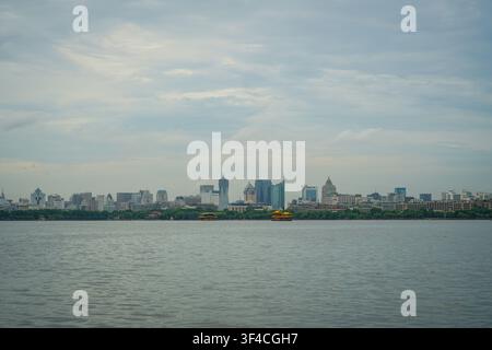 The West Lake features ripples across its grey-blue surface, with the Hangzhou city skyline visible along the distant shore, characterized by numerous Stock Photo