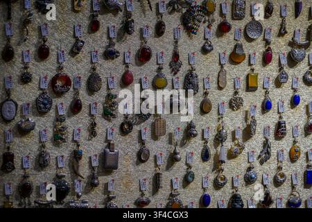 A textured gold fabric wall displays dozens of ornate pendants, each hanging individually from a small white tag with red text. The pendants vary wide Stock Photo
