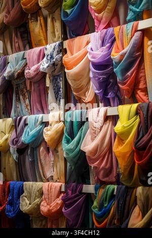 Dozens of lightweight, translucent scarves in various solid colors and patterned designs are draped and folded over three horizontal white metal rods, Stock Photo