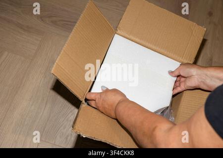 Close up of female hands removing foam protective layer from cardboard box. Concept: protective packaging industry  Stock Photo