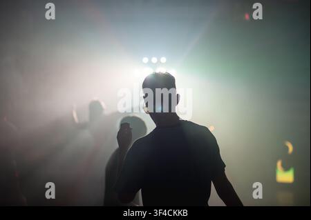 Backlit young man dancing at a music festival surrounded by fog and stage lights Stock Photo