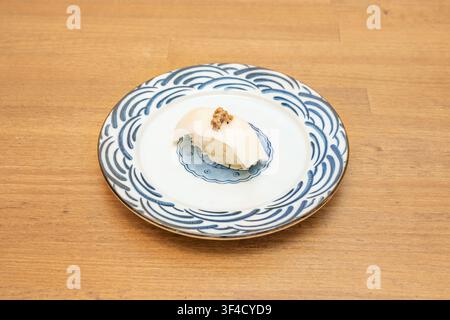 Single piece of white fish nigiri topped with a savory garnish, presented alone on an ornate blue wave-patterned plate. Stock Photo