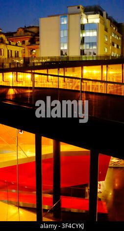 View from the rooftop terrace showing the glass facade with red interior structures and illuminated ramp inside the MACRO Museum. Rome, Italy. Stock Photo