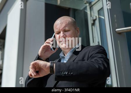 Businessman checking smartwatch during business phone call Stock Photo