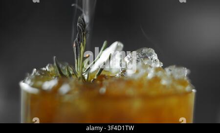Smoked rosemary sprig with crushed ice in an amber cocktail glass, showcasing a sophisticated beverage presentation Stock Photo
