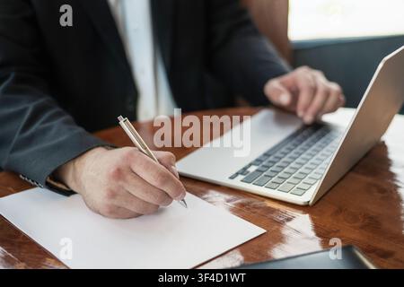 Businessman writing notes while working on laptop Stock Photo