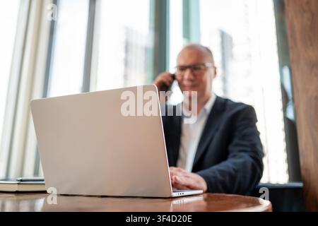 Businessman talking on smartphone while working on laptop in cafe Stock Photo