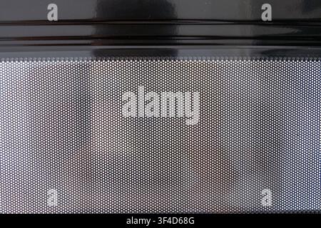 A detailed view of a black perforated metal screen, showing a uniform pattern of small holes against a blurred background Stock Photo