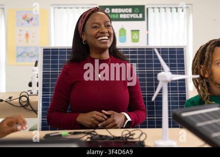 African American teacher with students showing solar panel wind turbine using tablet in classroom Stock Photo
