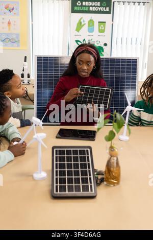 African American teacher with youths showing solar panel and turbines holding wires in classroom Stock Photo