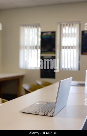 Silver laptop is sitting open on long white table in study room, with mustard chairs Stock Photo