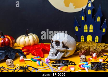Halloween decorations featuring a skull, sweet treats, and a haunted house on a yellow and black background Stock Photo