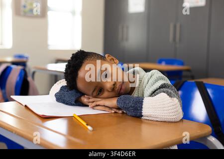African American child student sitting resting head on hands at classroom desk with open notebook Stock Photo