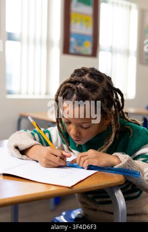 African American boy drawing with yellow pencil and blue ruler on open notebook at school desk Stock Photo