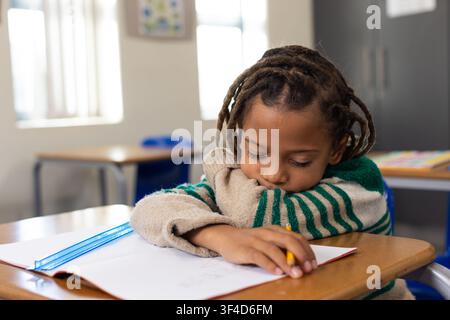 African American child resting on desk holding pencil over notebook in classroom with blue ruler Stock Photo