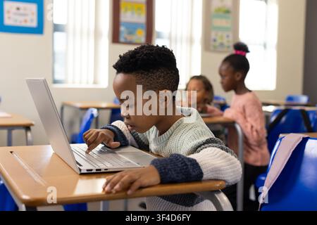 African American children with boy in striped sweater working on silver laptop at classroom desk Stock Photo