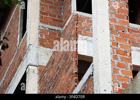 An unfinished brick building facade under construction with exposed red clay brick and concrete columns, textured pattern and industrial urban feel Stock Photo