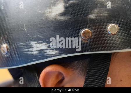 A worn black helmet with scuff marks and metal rivets over child ear, conveying outdoor action and protective gear in use Stock Photo