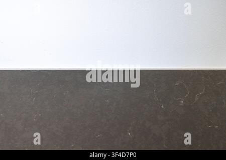 A minimalist abstract background featuring the texture of a dark stone surface meeting a clean white wall with a thin dividing line Stock Photo
