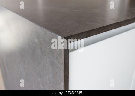A close-up view of a dark gray stone countertop edge meeting a clean white cabinet surface, showcasing material contrast and modern design Stock Photo