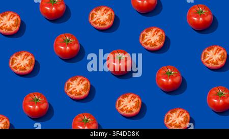 Whole and halved tomatoes arranged in pattern on dark blue background Stock Photo