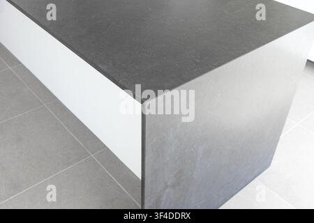 Close-up view of a contemporary kitchen island featuring a dark textured countertop and a clean white base, set against tiled flooring Stock Photo