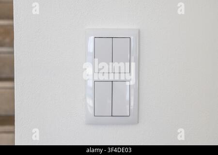 A clean and minimalist electrical switch panel featuring four distinct buttons, mounted on a subtly textured white wall surface Stock Photo