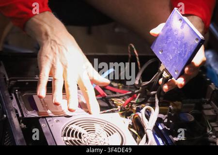 A person installs a blue graphics card into a desktop computer tower. Close up of internal components, wires, and cooling fan. Sharp focus on the hard Stock Photo