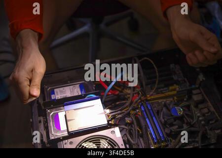 A person works on a desktop computer by connecting internal components including a graphics card, memory sticks, and cables. Detailed view of the inte Stock Photo