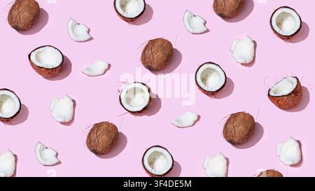 Whole and halved coconuts arranged in pattern on pastel pink background Stock Photo