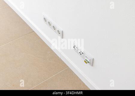A clean white wall features multiple electrical sockets and a network data port with a yellow connector inserted Stock Photo