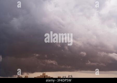A dramatic and moody cinematic shot of heavy storm clouds gathering across the sky. The natural weather scene displays intense dark gray textures and Stock Photo