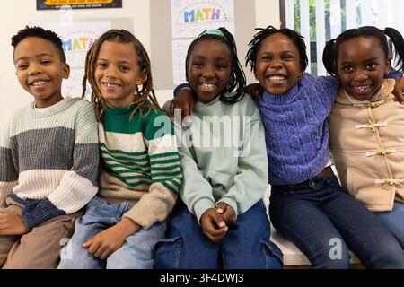African American youth students sitting on bench in classroom, smiling at camera with MATH poster Stock Photo