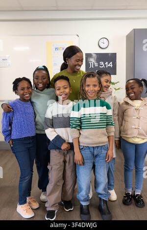 African American woman teacher with students standing at front of classroom near whiteboard Stock Photo