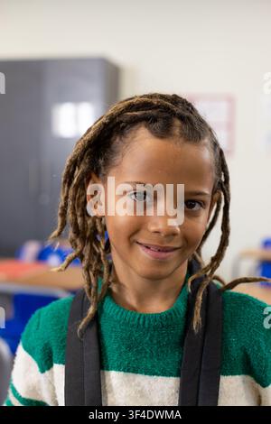 African American male child smiling, sitting at school wearing green sweater and backpack straps Stock Photo
