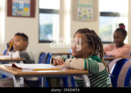 African American children sitting at desks in bright classroom with notebooks and pencils Stock Photo