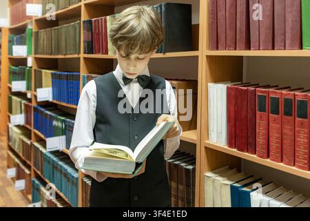 Schoolboy in school uniform, deeply focused on reading book in library Stock Photo