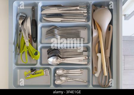 Top view of organized kitchen drawer filled with cutlery, utensils, scissors and accessories in plastic divider tray Stock Photo
