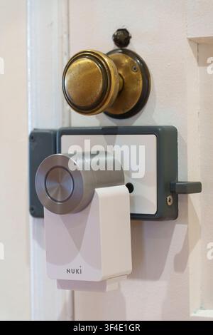 Nuki smart lock installed on a wooden door beneath a traditional brass doorknob Stock Photo