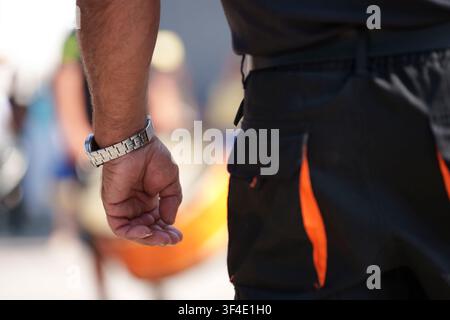 Close-up view of a man's arm and hand wearing a metallic wristwatch while standing outdoors Stock Photo