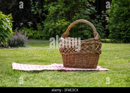 Empty wicker picnic basket on blanket in green garden with copy space Stock Photo