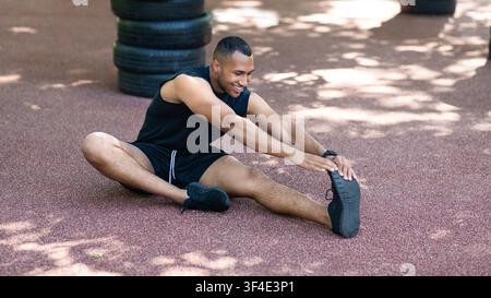 Handsome black guy in sportswear stretching his leg muscles after his jogging at park Stock Photo