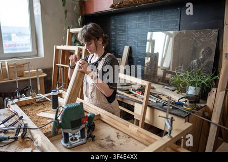 Skilled concentrated female carpenter carefully measuring wooden board with ruler in repair shop. Stock Photo