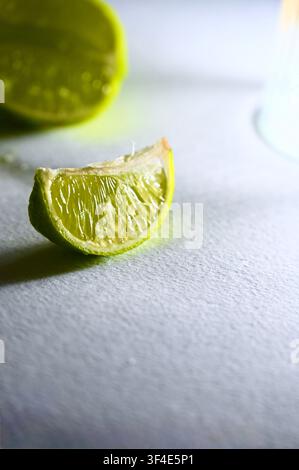 Close-up shot of a fresh lime wedge casting a long shadow on a light grey textured paper surface. Studio lighting highlights the juicy pulp detail. Perfect for culinary, beverage, minimalist food photography, and healthy concept layouts. Stock Photo